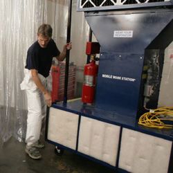 Painter moving portable automotive paint booth in body shop.