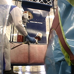 Painter in portable spray booth spraying auto fender.