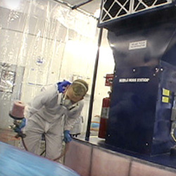 Painter spraying fender using portable paint booth in body shop.