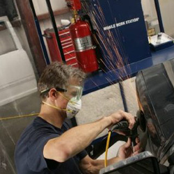 Man grinding automobile fender in portable paint prep station.